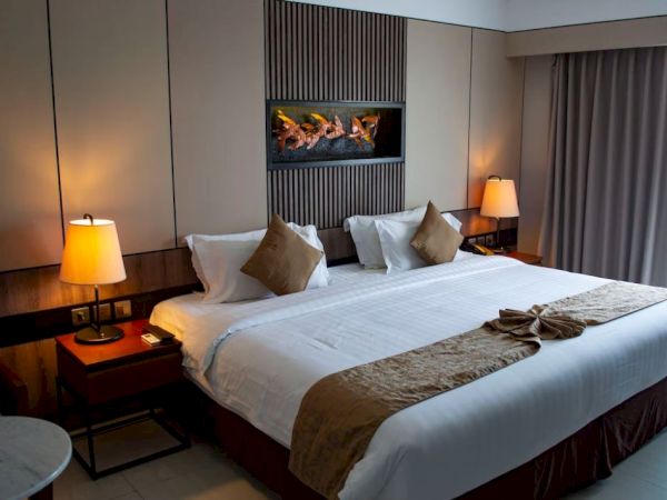 A cozy hotel room with a large bed, bedside lamps, and a decorative piece above the headboard. A curtain covers the window.