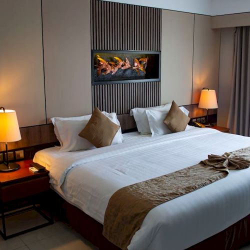 This image shows a well-decorated hotel room with a large bed, two bedside tables with lamps, and a small table with chairs in the corner.