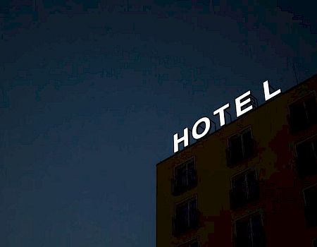 The image shows the exterior of a building at night with a lit sign that reads "HOTEL." The letters are on the top of the building.