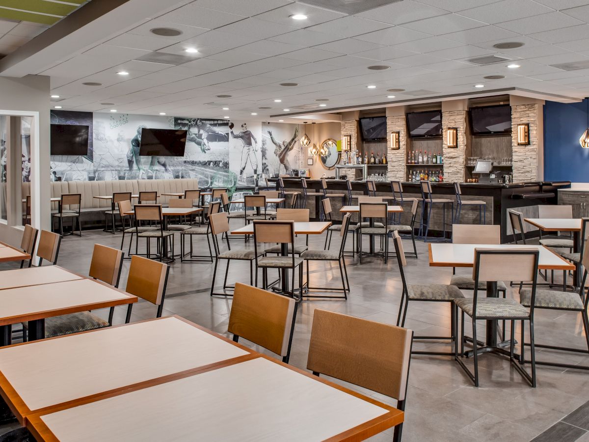 A modern, empty restaurant with neatly arranged tables and chairs, a bar area in the back, and multiple TVs mounted on the walls.