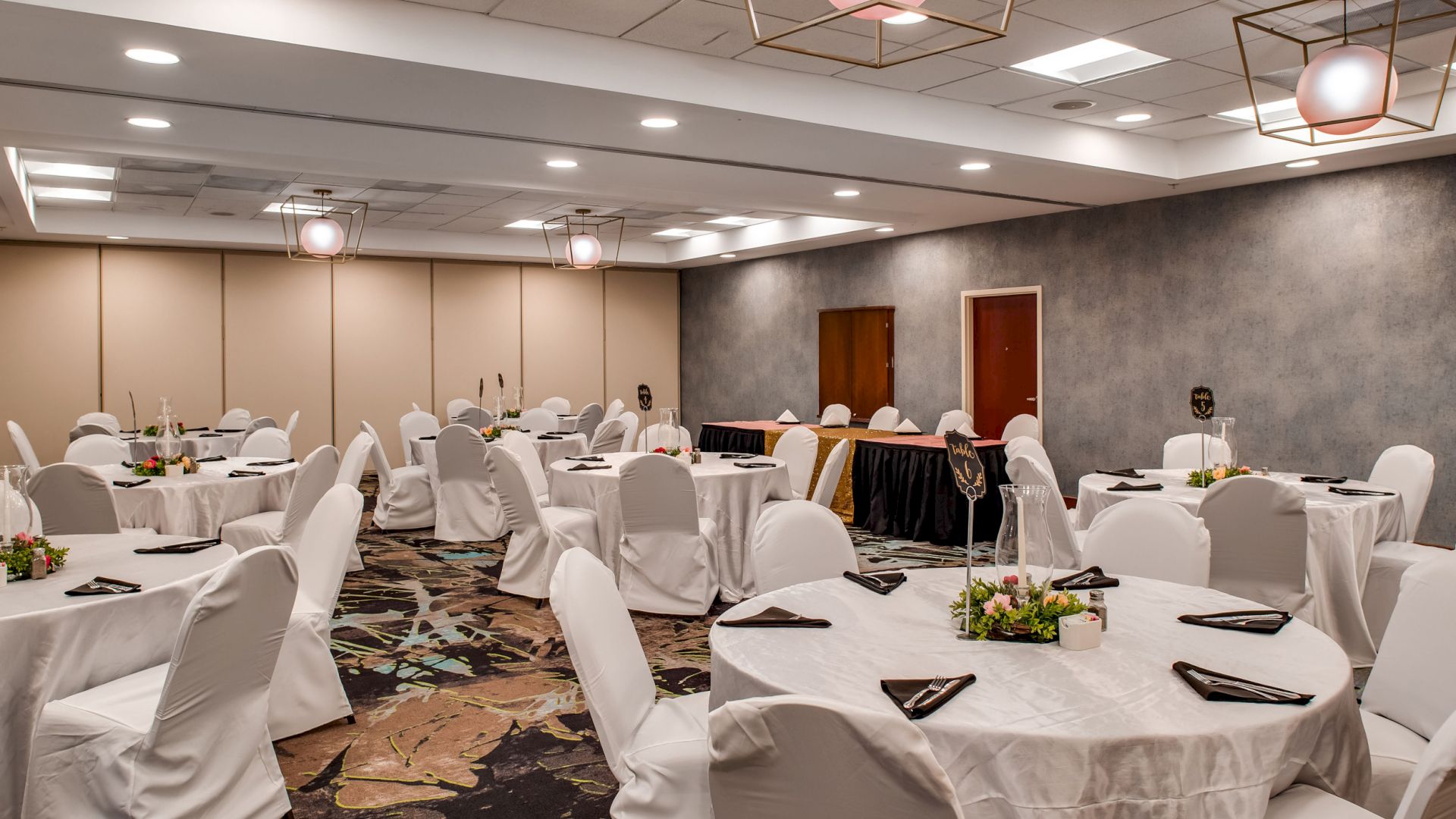This image shows a banquet hall set up with round tables and white tablecloths, adorned with floral centerpieces and napkins, ready for an event.