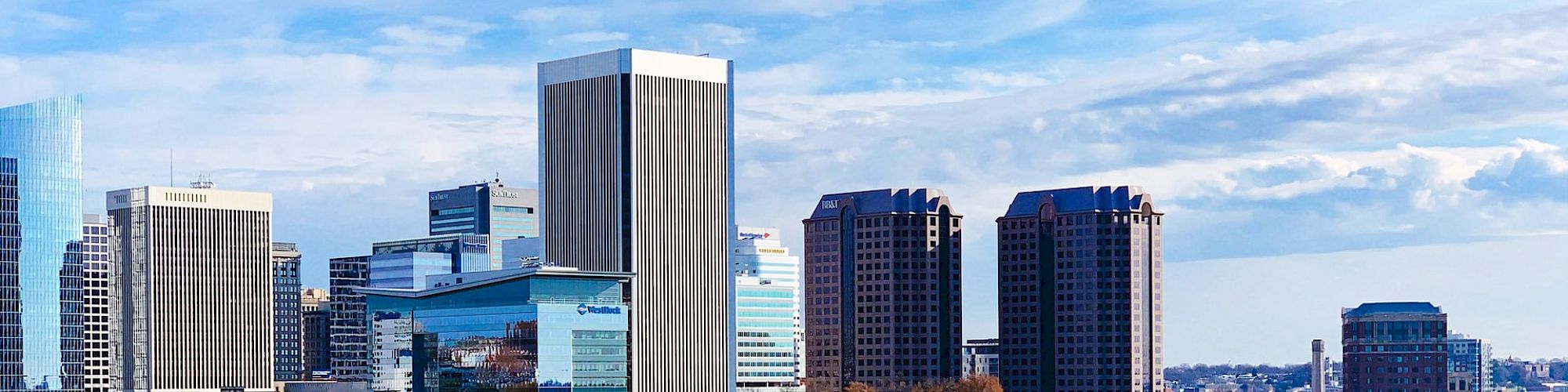 A cityscape with modern high-rise buildings, a river, and a bridge, featuring a mix of urban and natural elements against a blue sky.