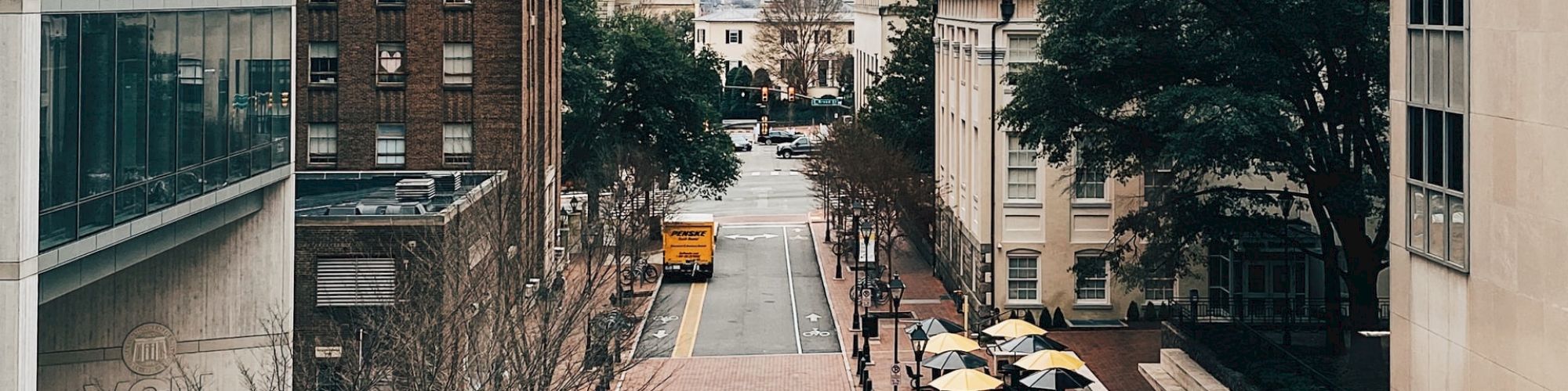 The image shows an urban street between tall buildings, partly cloudy sky, bike lanes, parked cars, and a truck entering a covered area.