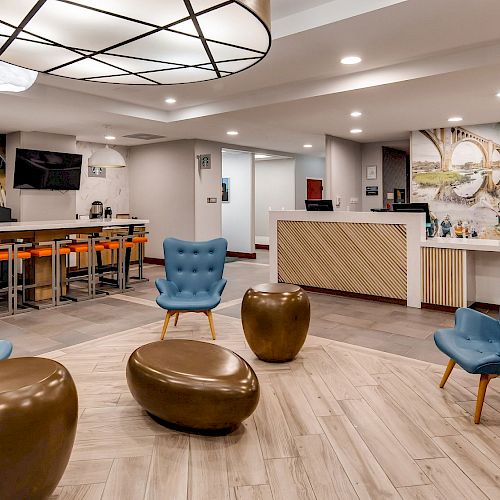 A modern lobby area with blue chairs, round ottomans, a front desk, wall art, and a bar with stools.