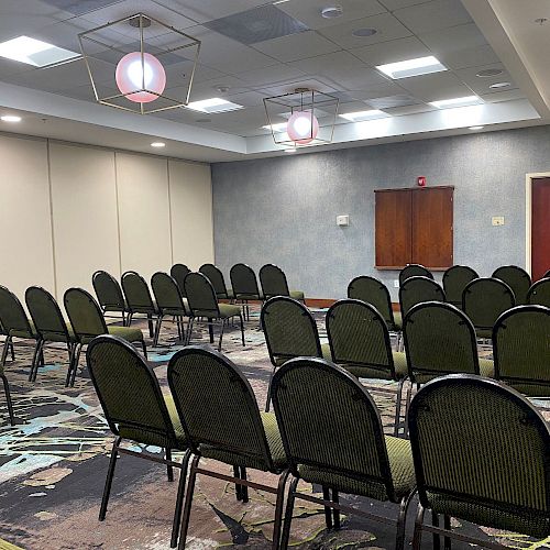 A room set up with rows of green chairs facing the front, likely for a presentation or meeting, with modern lighting and carpeted flooring.