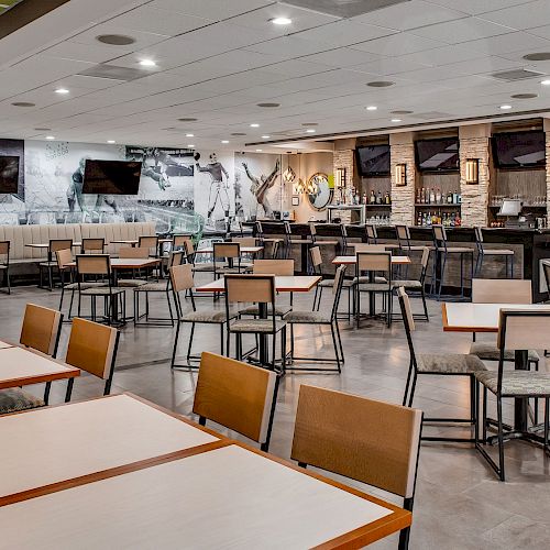 This image shows a modern, well-lit dining area with neatly arranged tables and chairs. There's a large bar counter in the background.