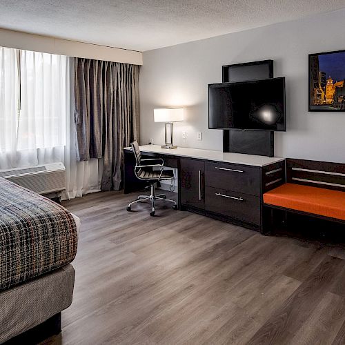 A modern hotel room with a bed, desk, chair, flat-screen TV, microwave, and seating area under a picture frame near the window ending the sentence.