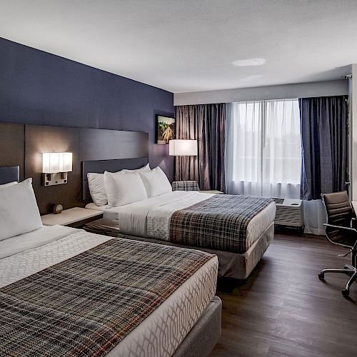 This image shows a modern hotel room with two beds, a desk with a chair, a TV, lamps, and a window with curtains.