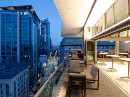 An outdoor terrace with seating overlooks a city street and tall buildings at dusk, creating a modern and urban ambiance.