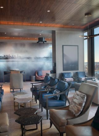 A modern lounge with ample seating, large windows offering a scenic view, soft ambient lighting, and a mural on the back wall.