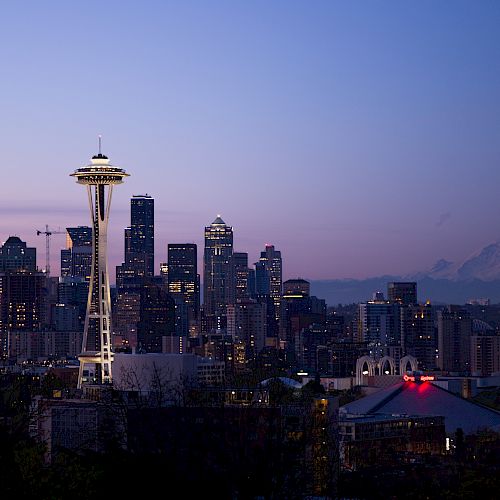 A night view of Seattle's skyline, featuring the Space Needle prominently in the foreground, with Mount Rainier visible in the background.