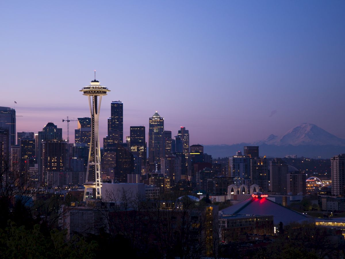 This image shows a cityscape at dusk with notable landmarks including the Space Needle and Mount Rainier in the background.