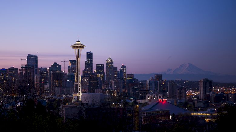 This image shows a cityscape at dusk with notable landmarks including the Space Needle and Mount Rainier in the background.
